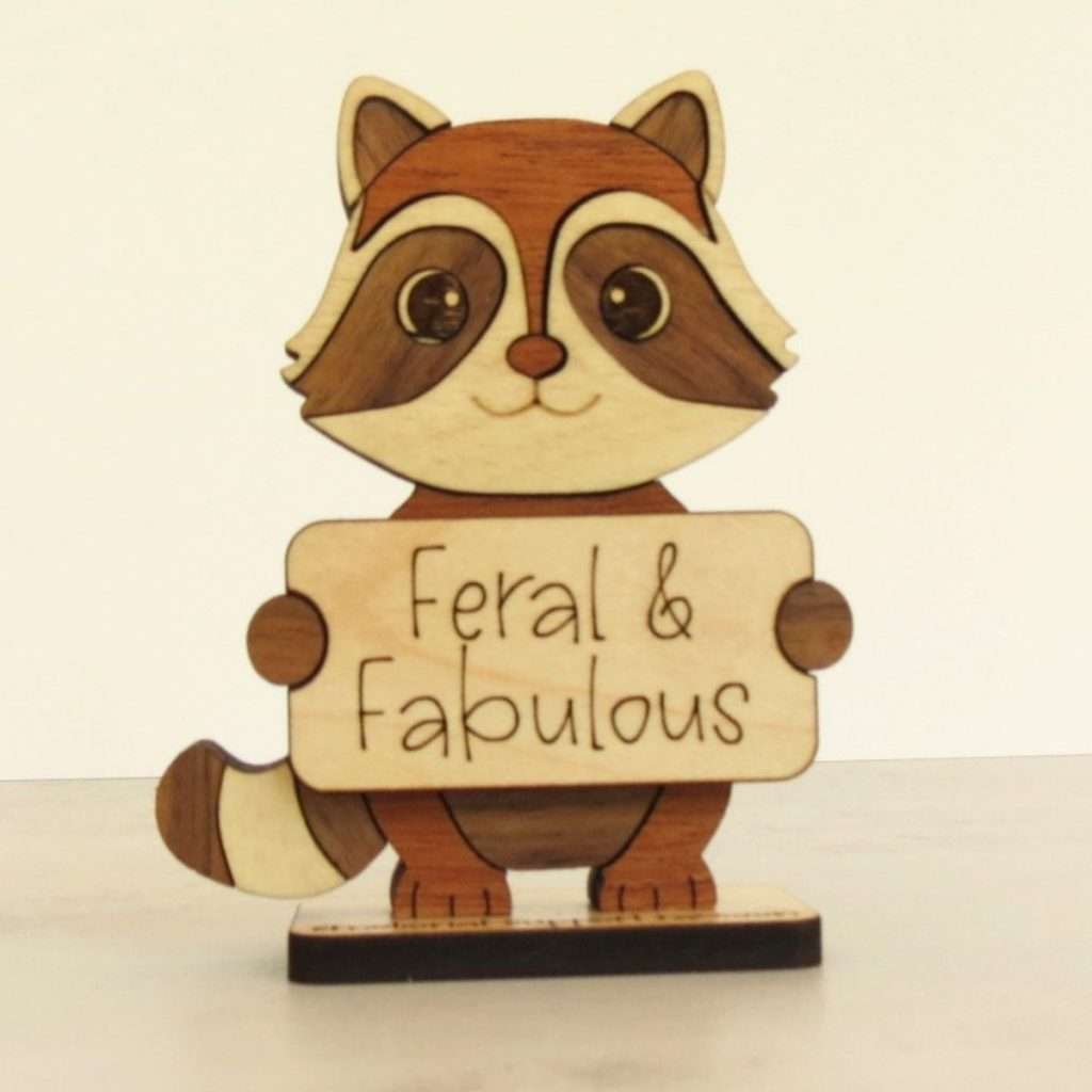Handcrafted hardwood emotional support raccoon desk pet holding sign that reads Feral and Fabulous