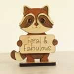 Handcrafted hardwood emotional support raccoon desk pet holding sign that reads Feral and Fabulous