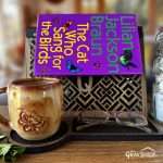 Geometric monogram book stand, shown in the dark stain and leather combination with the letter Qcutout in a styled scene with a novel and attractive handmade coffee mug. The mug is from a maker in Alabama.